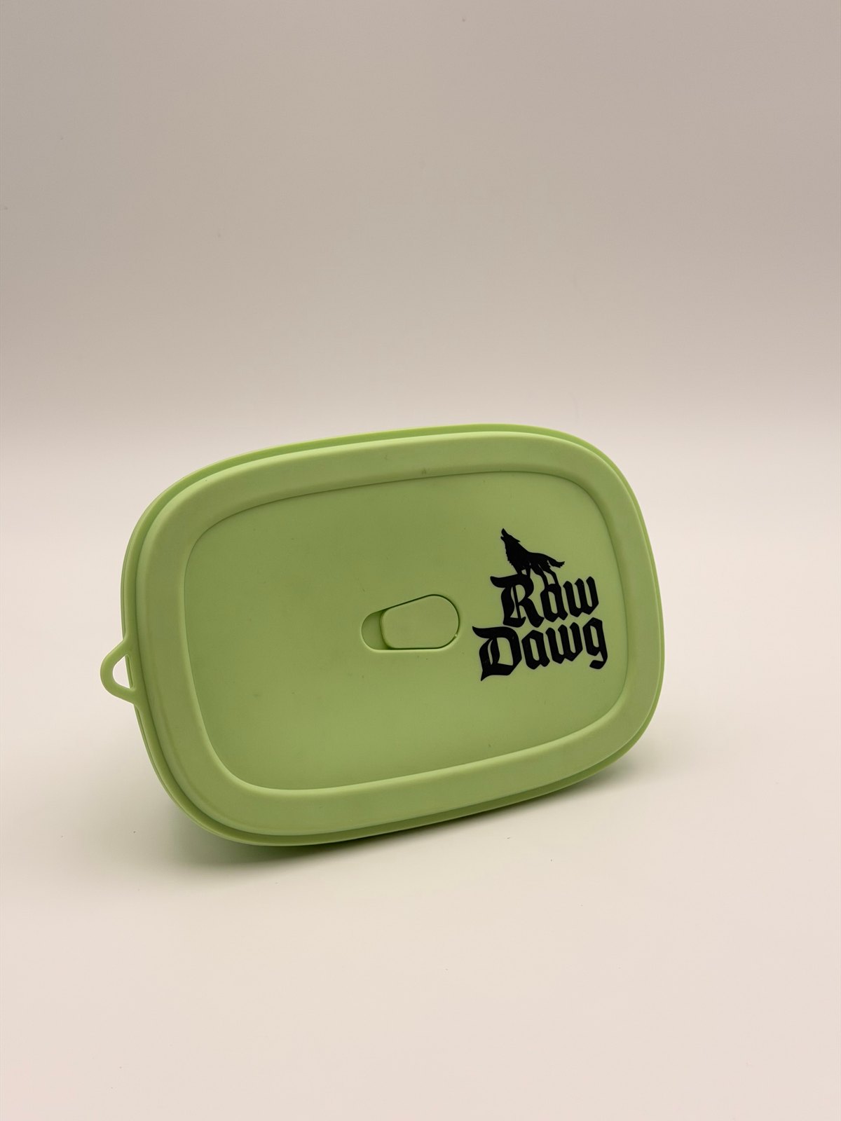 A closed green Raw Dawg food-storage container on a cream background.